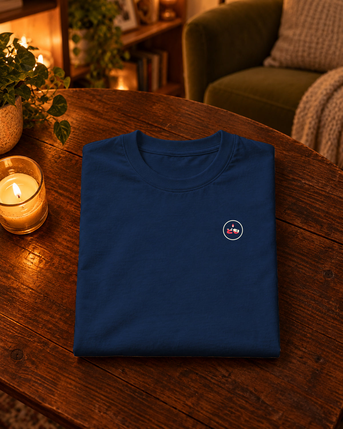 Kata Tee 型 | Candle — Navy — gevouwen kledingstuk met origineel borstlogo op een tafel thuis bij kaarslicht