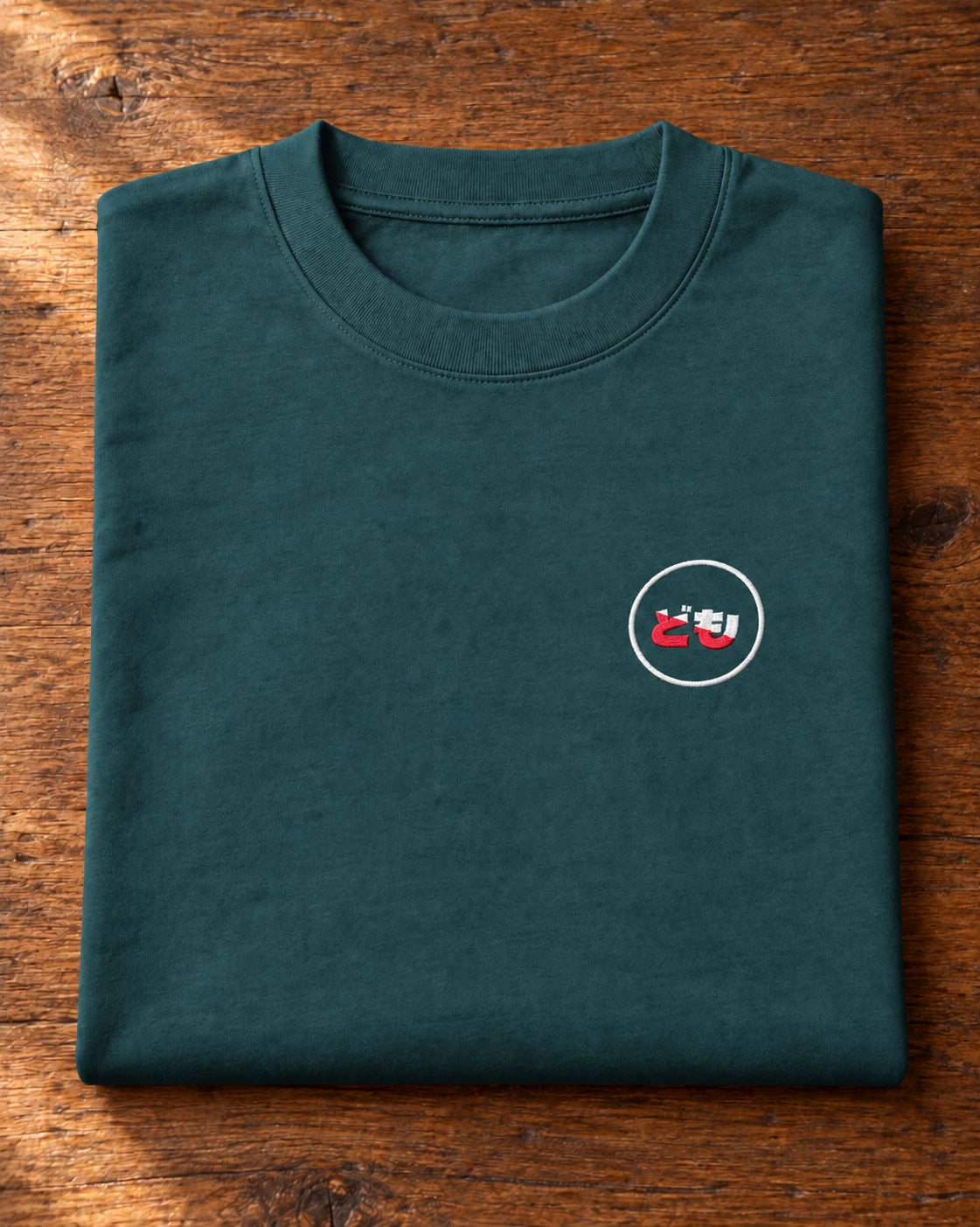 Kata Tee Embroidered 型 | Ink — folded shirt showing the embroidered Domo chest logo