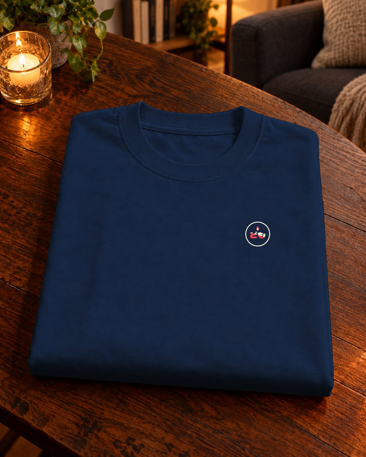 Fudō Tee 不動 | Candle — Navy — gevouwen kledingstuk met origineel borstlogo op een tafel thuis bij kaarslicht