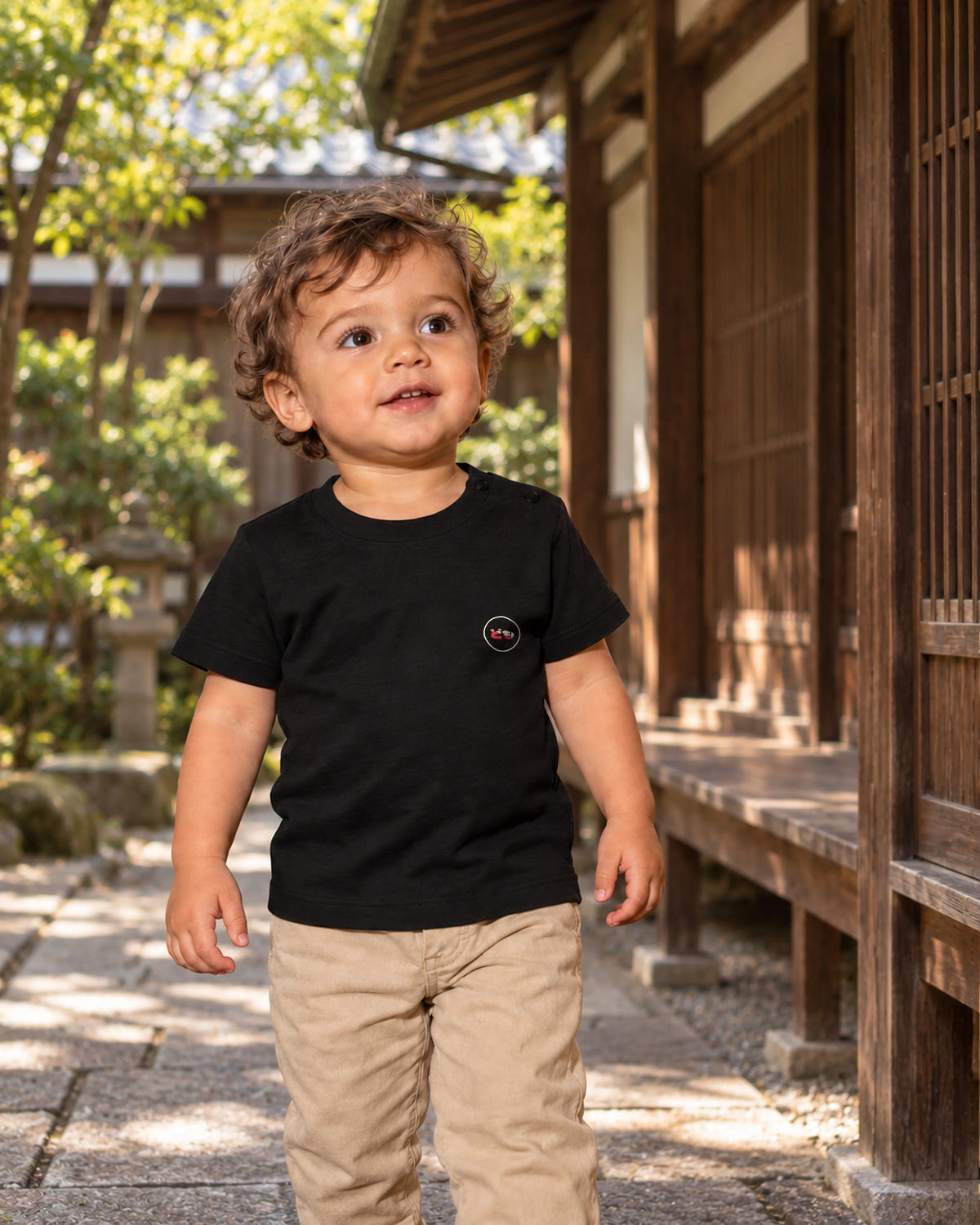 Hina Baby Tee 雛 | Ink — front view showing the Domo chest logo in a Japanese wooden courtyard