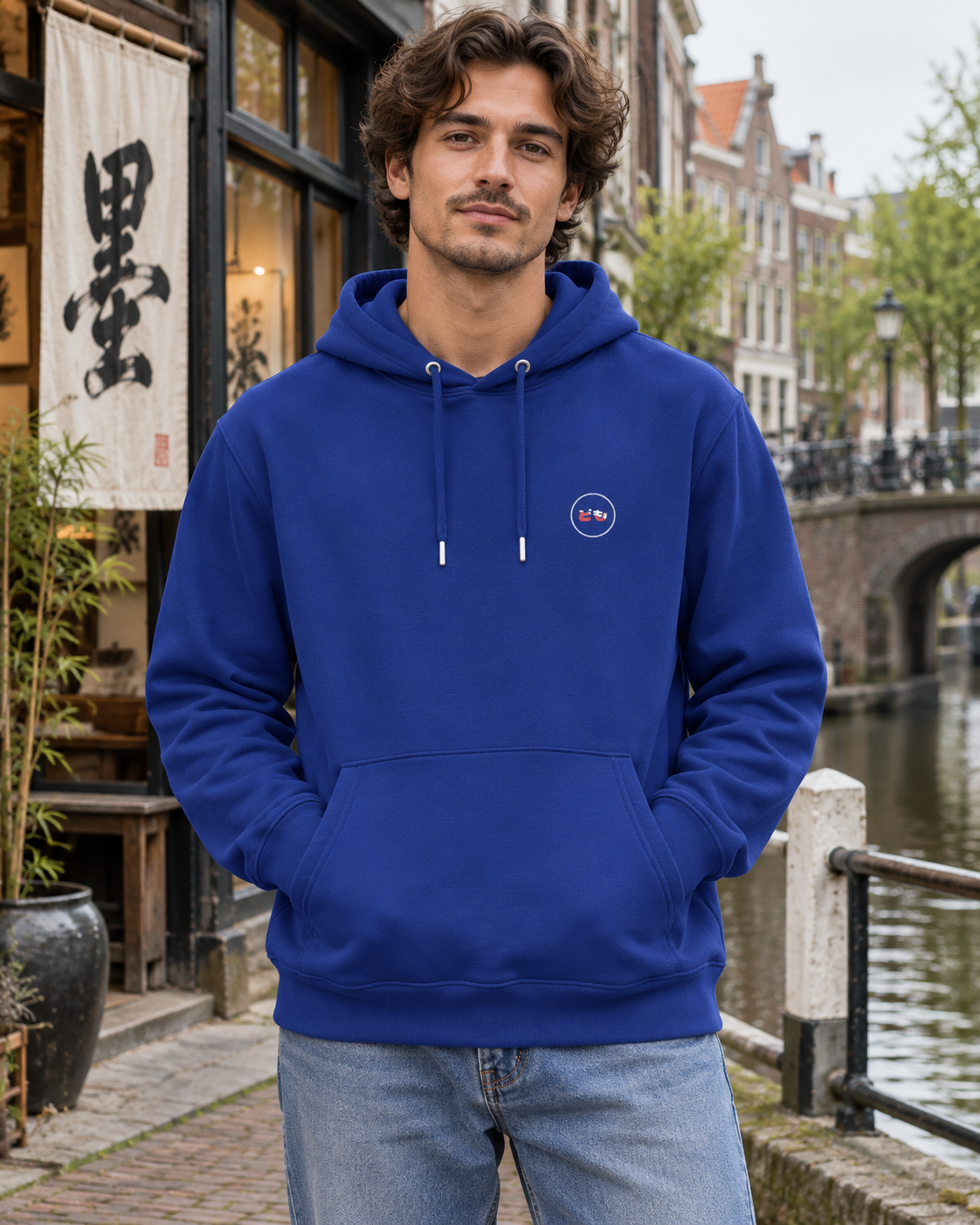 Nukumori Cruiser 2.0 350 GSM organic cotton fleece hoodie: RELAXED MEDIUM FIT, roomy chest and upper arms, shoulders gently relaxed, loose straight body and natural drape, comfortable streetwear, NOT slim or tight, NOT extreme oversized — Ink — front logo on model