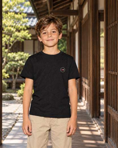 Wakaba Kids Tee 若葉 | Ink — front view showing the Domo chest logo in a Japanese wooden courtyard
