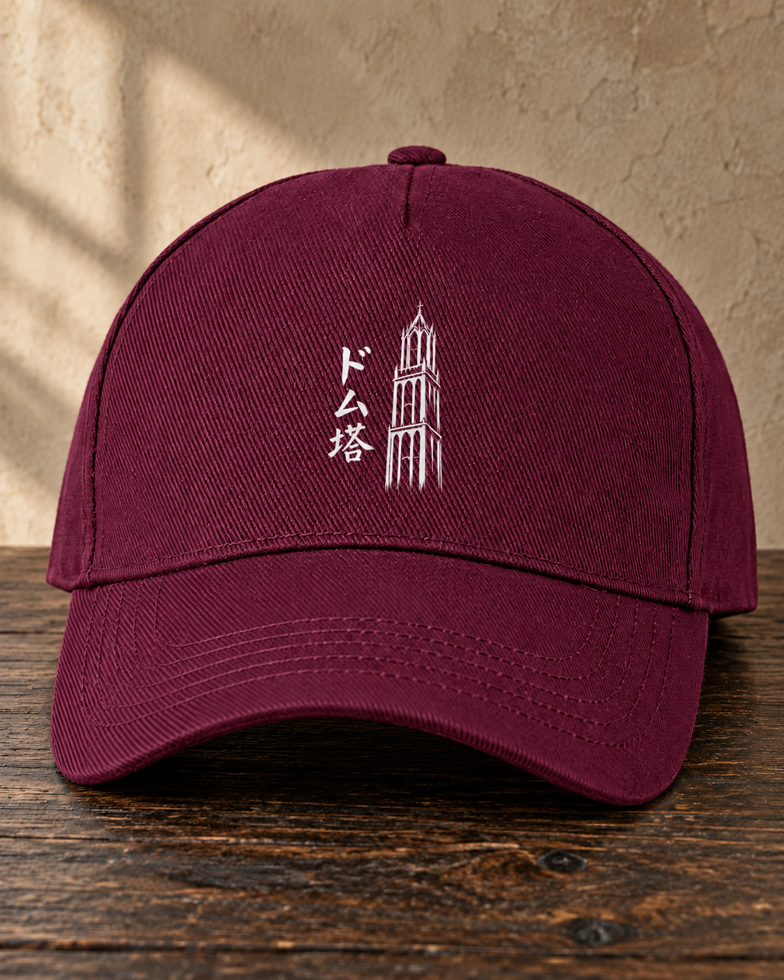 Kage Cap 影 | Burgundy — vooraanzicht met wit Ink-ontwerp op een houten tafel