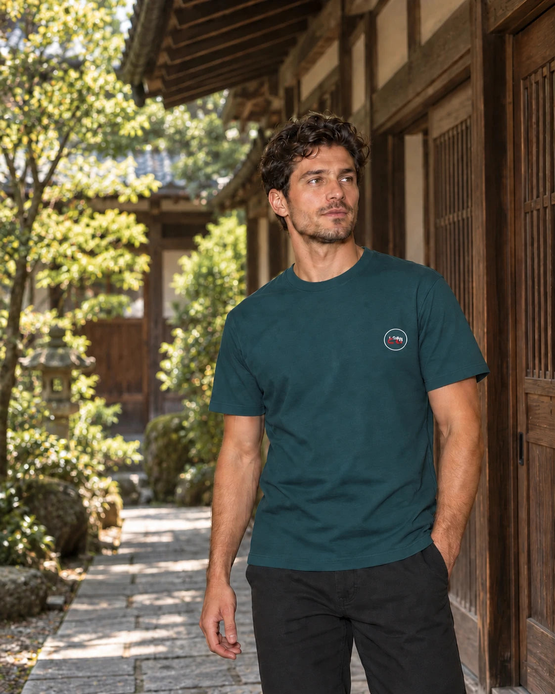 Kata Tee Embroidered 型 | Ink — front view showing the embroidered Domo chest logo in a Japanese courtyard